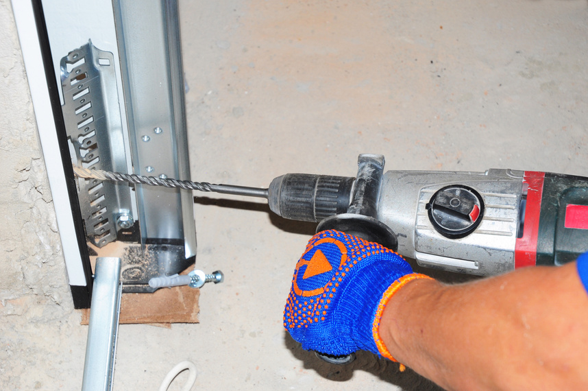 Contractor  repair and install garage door with drilling machine. Replace a broken garage door spring.